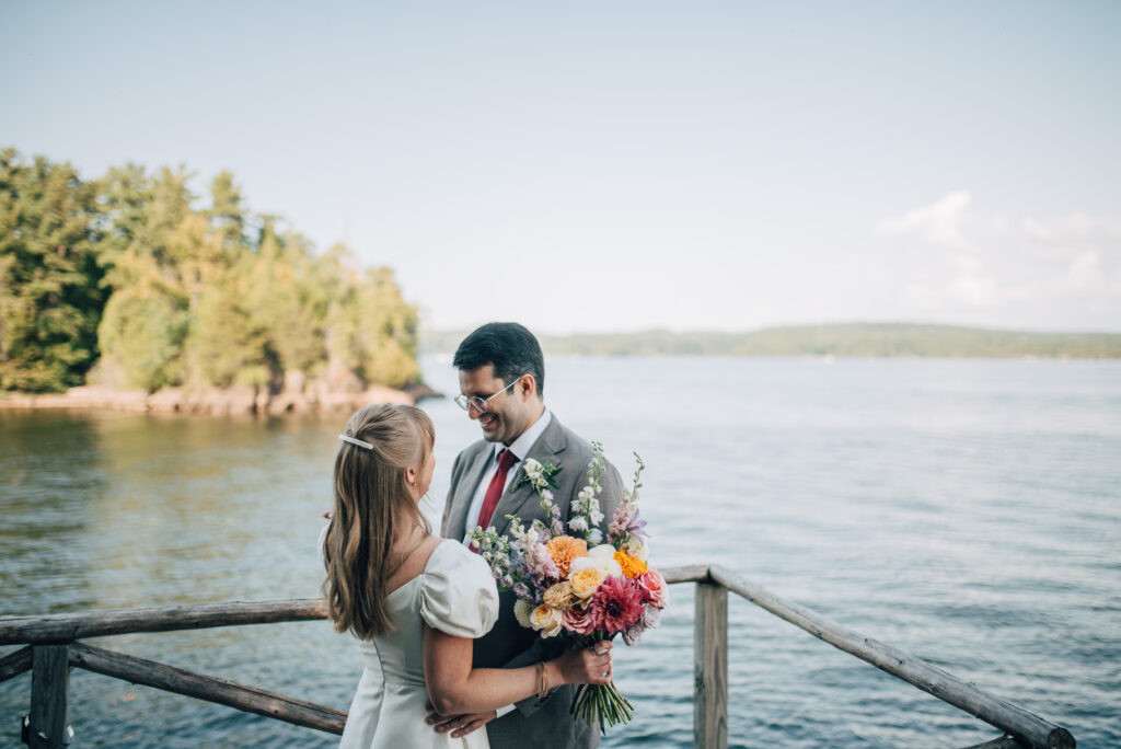A wedding couple standing on a dock, gazing at each other along Lake Champlain.